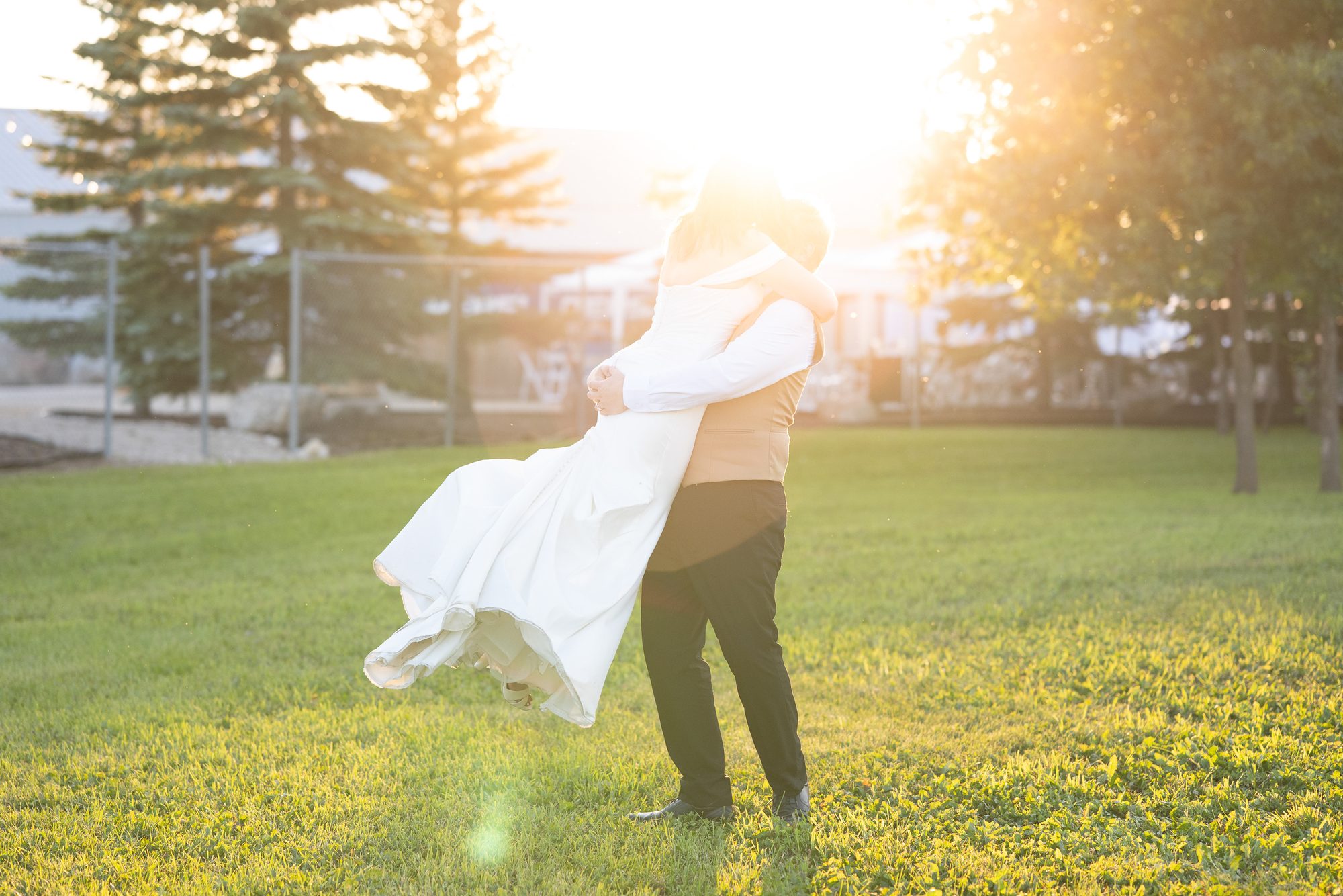 Groom lifting bride at golden hour on the grass at Little Mountain Sportsplex, Winnipeg